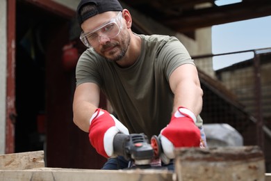 Man polishing wooden planks with angle grinder outdoors