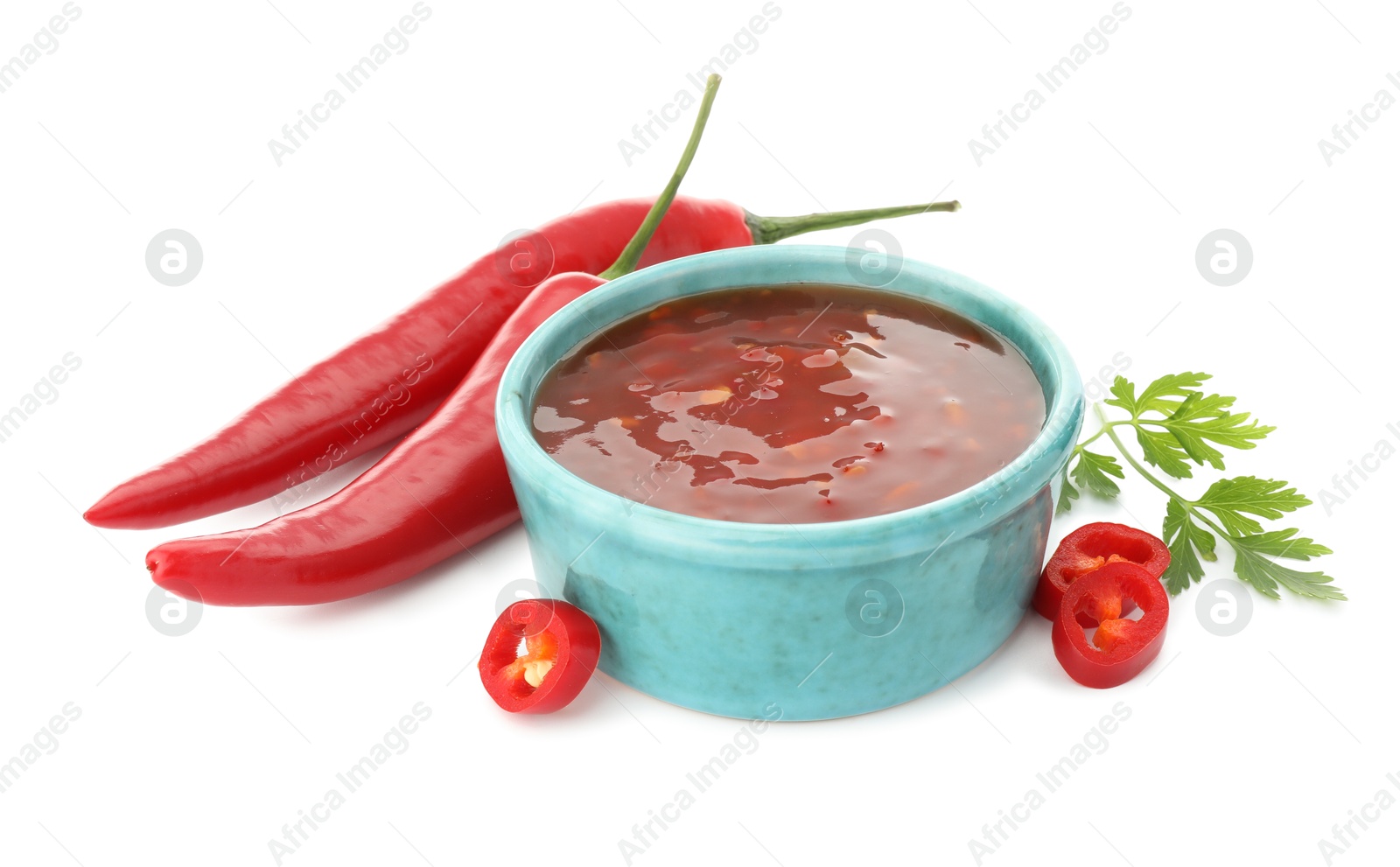 Photo of Hot chili sauce in bowl, parsley and peppers isolated on white