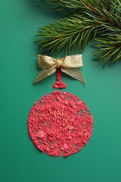 Christmas ball made of blush with bow and fir branch on green background, top view