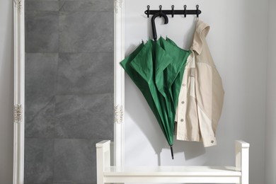 Photo of Green umbrella and jacket on hanger near mirror indoors