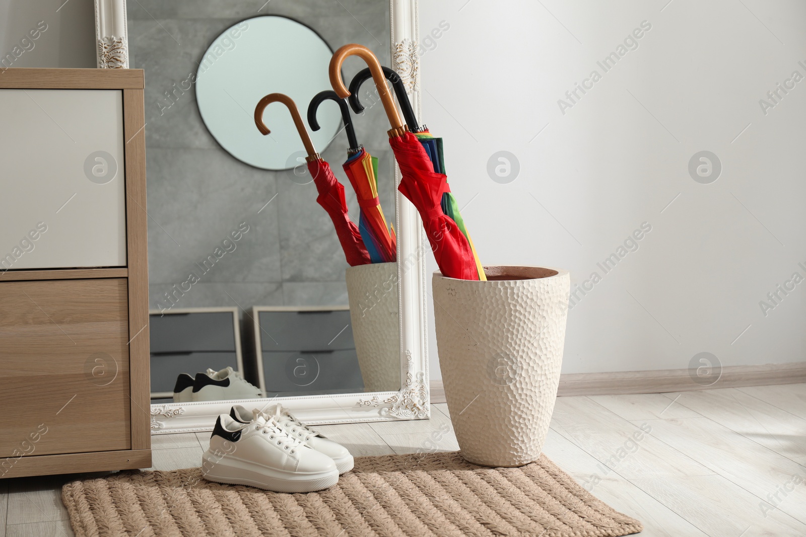 Photo of Holder with bright umbrellas, mirror and cabinets in hallway