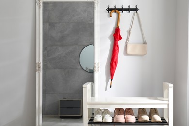 Photo of Red umbrella and bag on hanger near mirror over shoe storage bench indoors