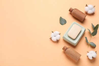 Photo of Different cosmetic products, leaves and cotton flowers on pale orange background, flat lay. Space for text