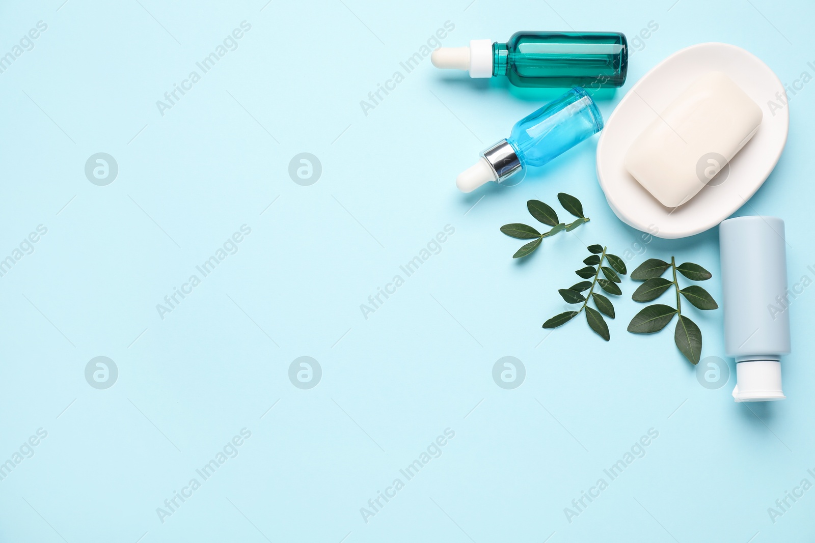 Photo of Different cosmetic products and leaves on light blue background, flat lay. Space for text