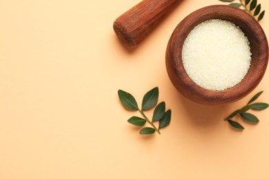 Photo of Cosmetic product. Sea salt and green leaves on pale orange background, flat lay. Space for text