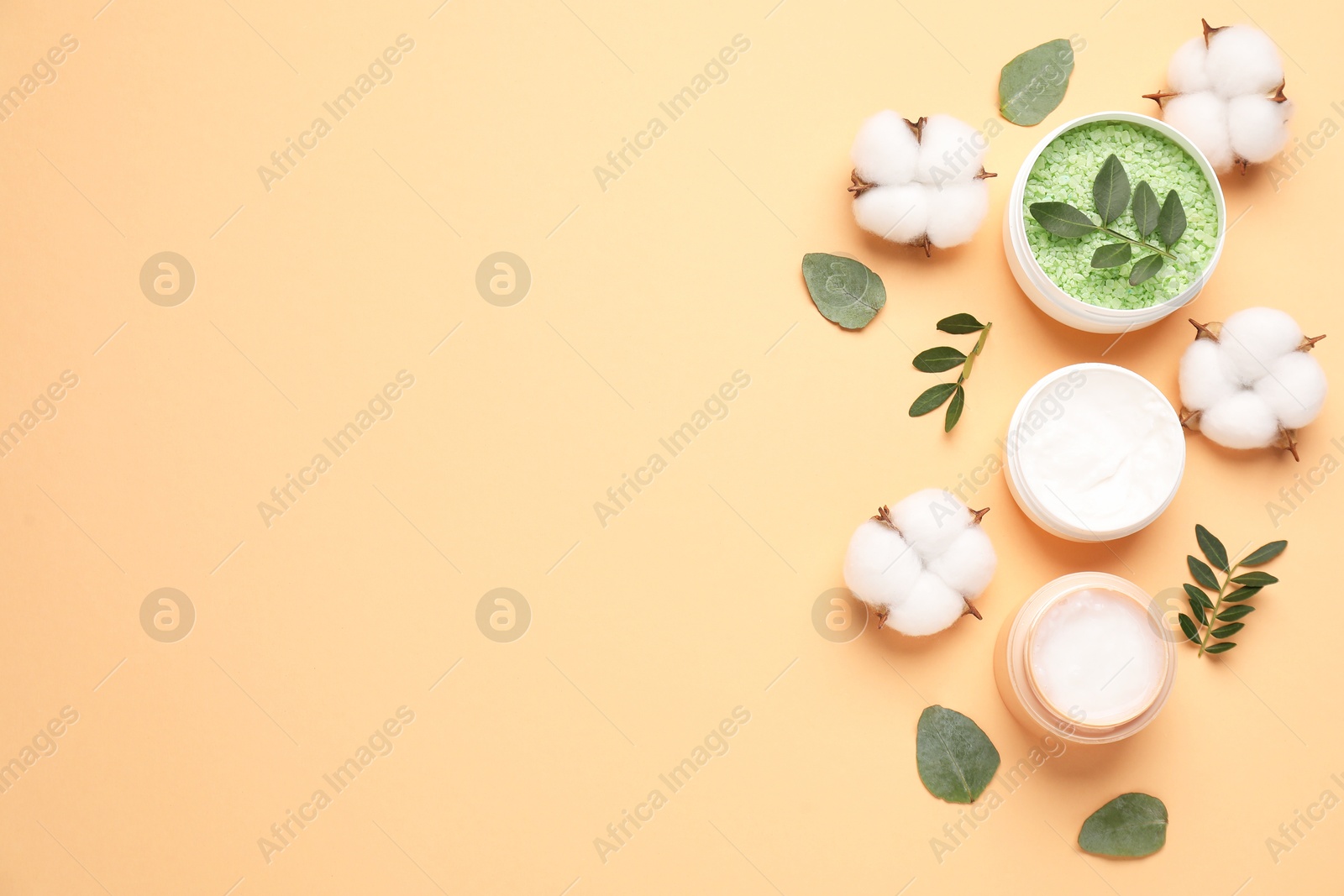 Photo of Different cosmetic products, cotton flowers and green leaves on pale orange background, flat lay. Space for text