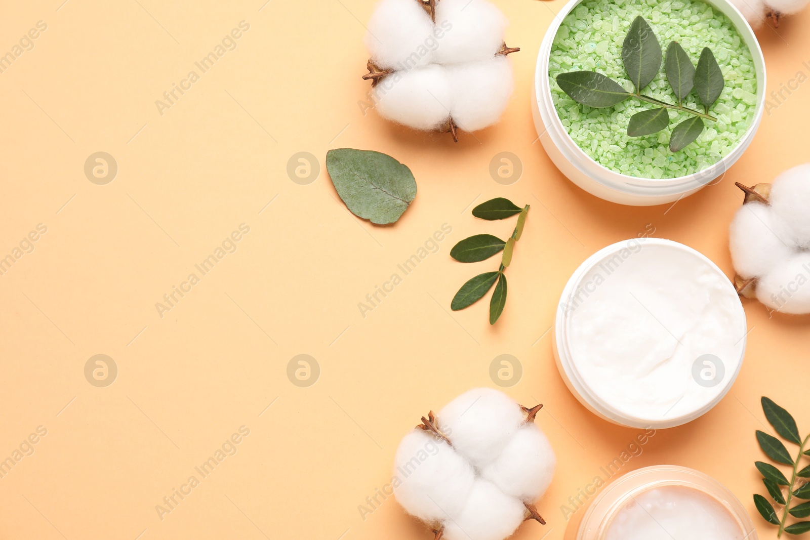 Photo of Different cosmetic products, cotton flowers and green leaves on pale orange background, flat lay. Space for text