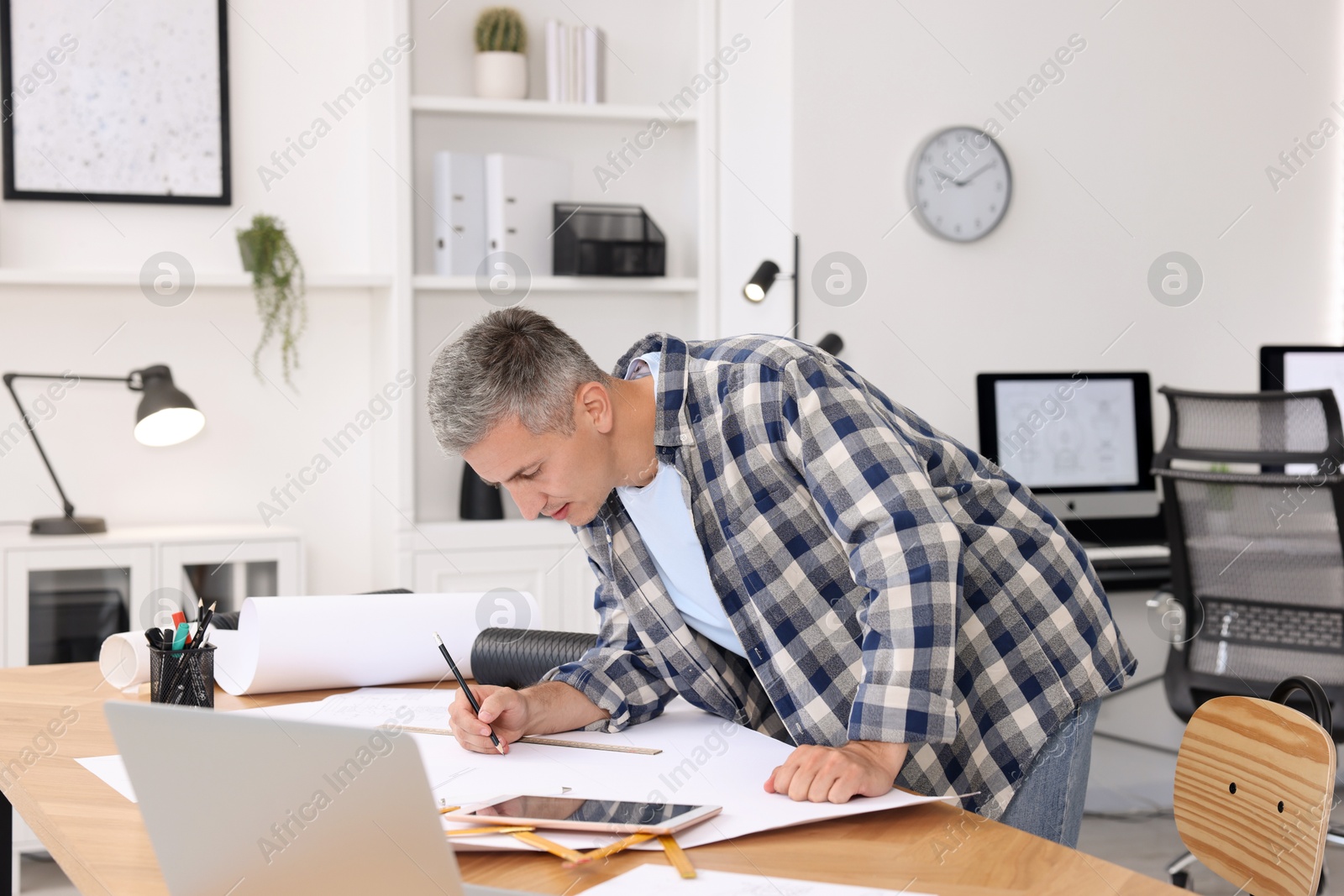 Photo of Architect making engineering drawing at wooden table in office