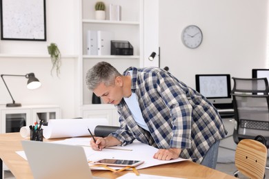 Photo of Architect making engineering drawing at wooden table in office