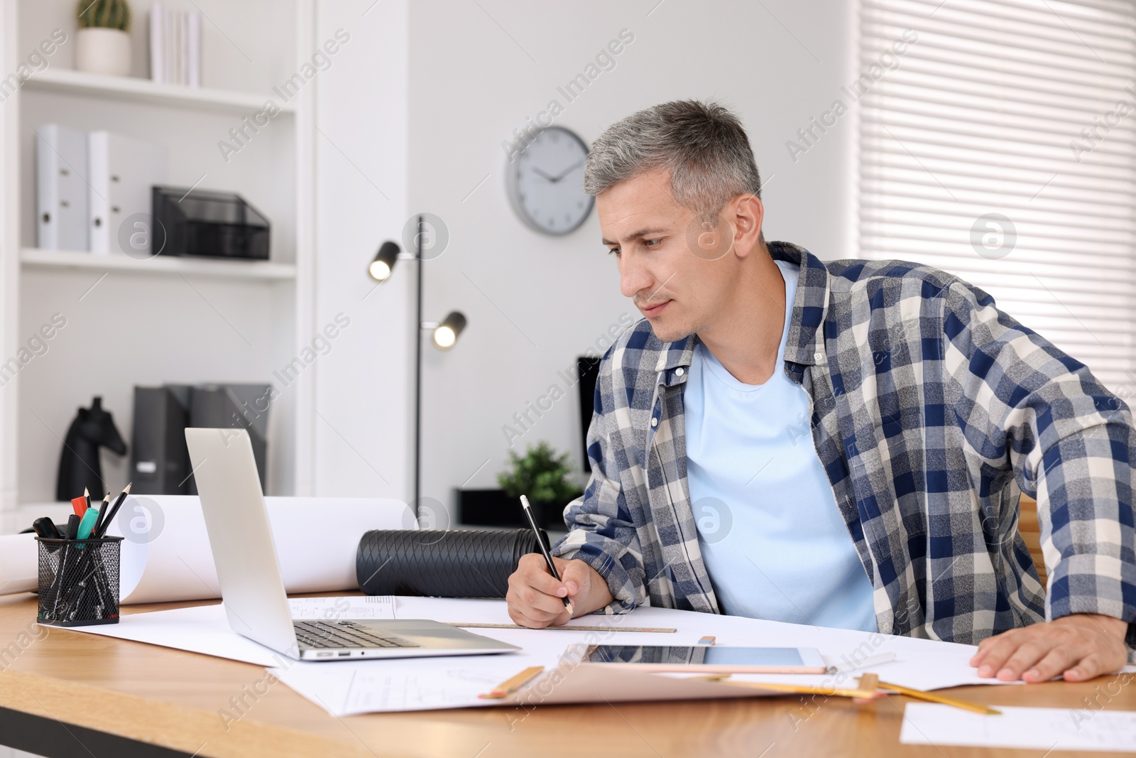 Photo of Architect making engineering drawing at wooden table in office