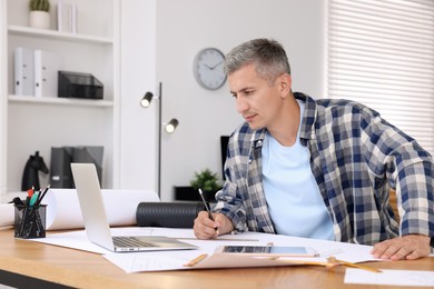 Architect making engineering drawing at wooden table in office