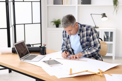 Photo of Architect making engineering drawing at wooden table in office