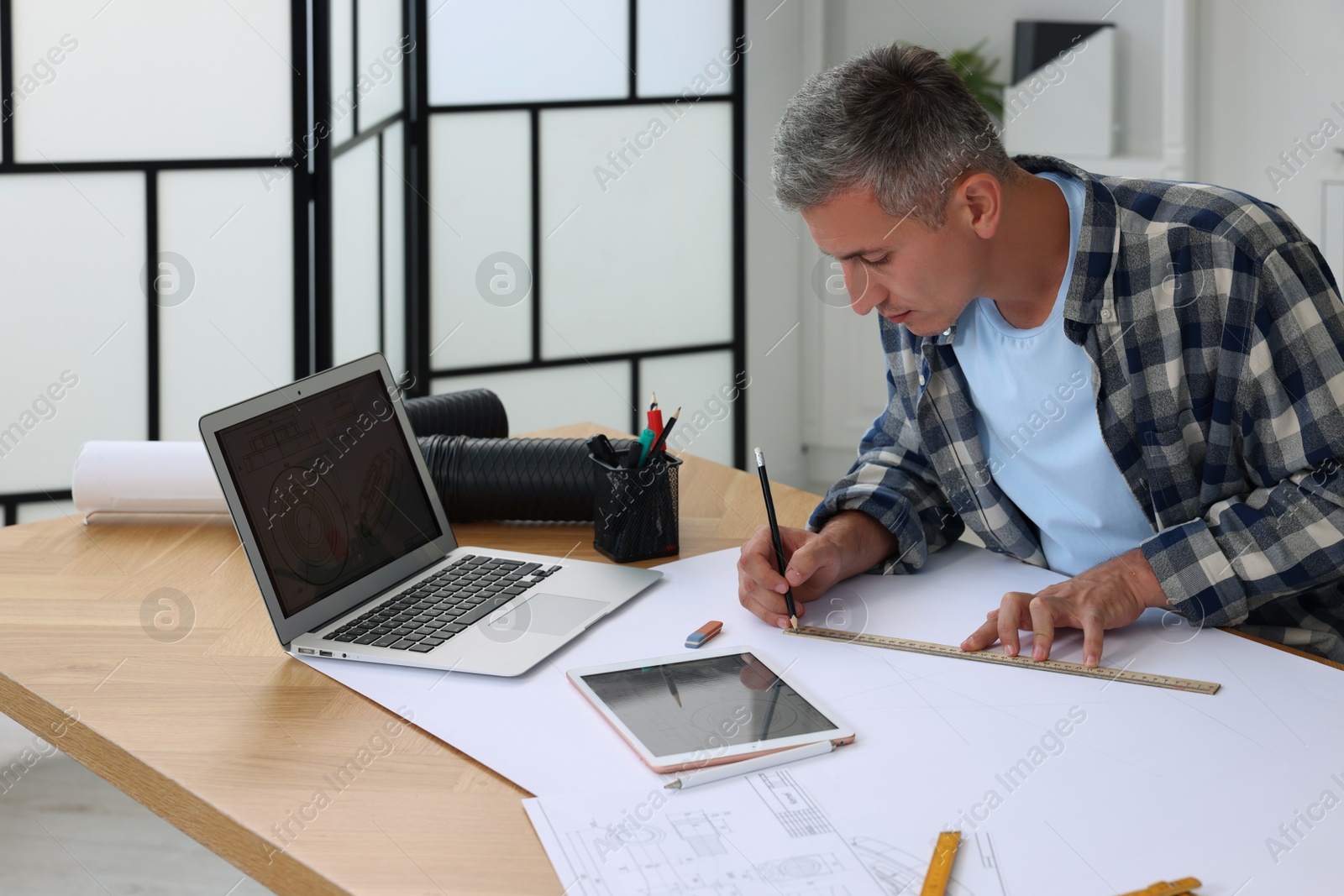 Photo of Architect making engineering drawing at wooden table in office