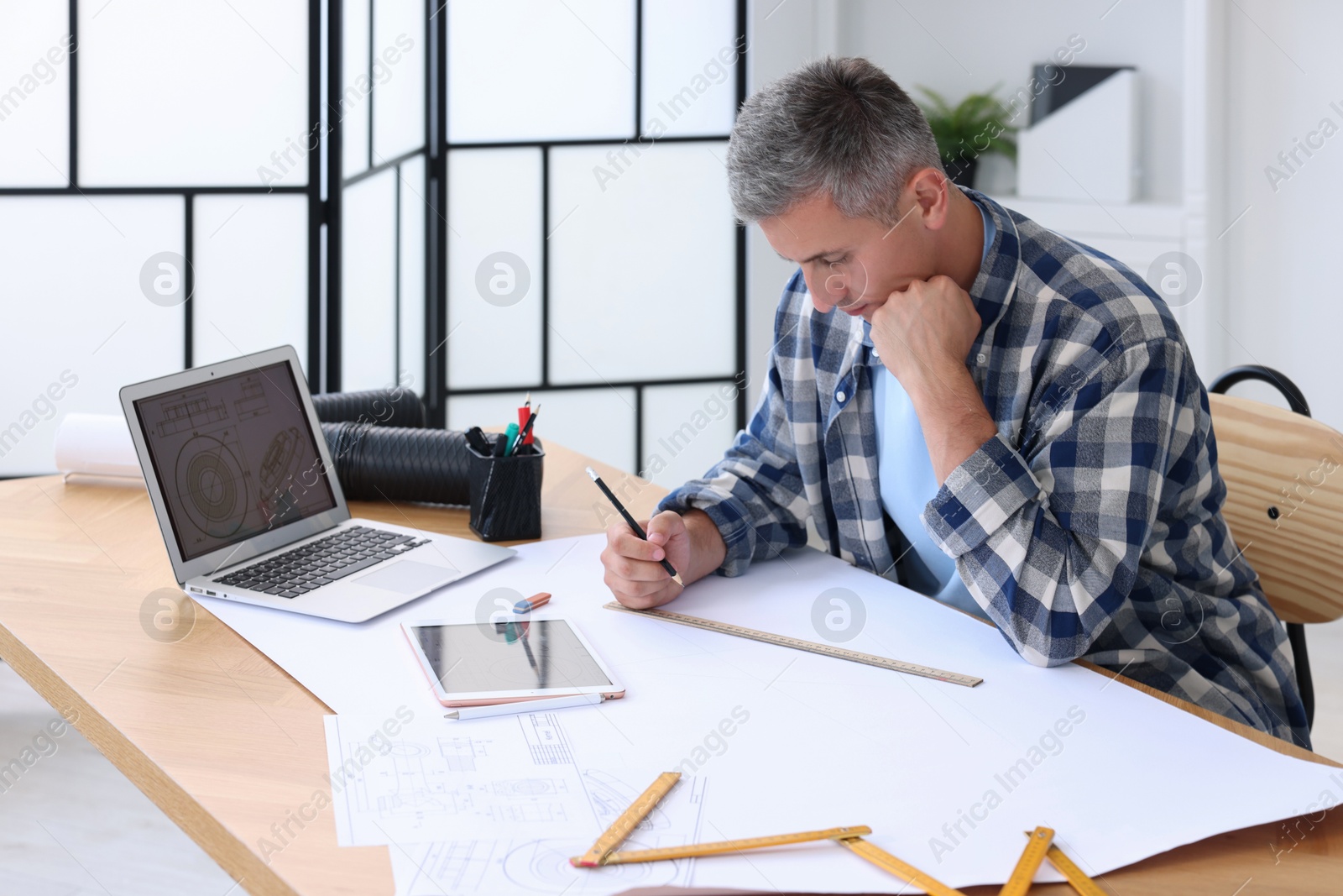 Photo of Architect making engineering drawing at wooden table in office