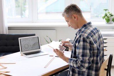 Photo of Architect making digital engineering drawing on tablet at table in office