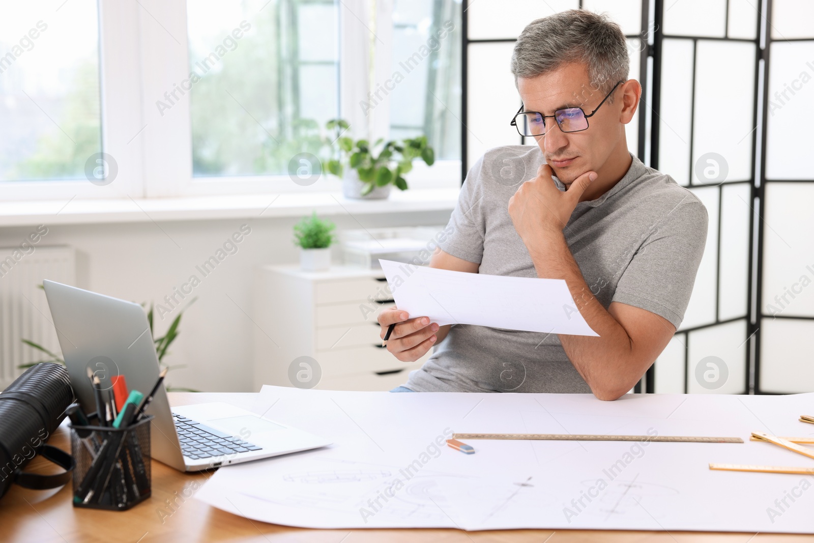 Photo of Architect with engineering drawing at wooden table in office