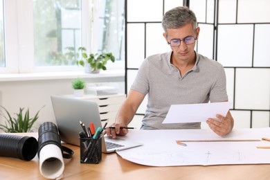 Photo of Architect with engineering drawing at wooden table in office