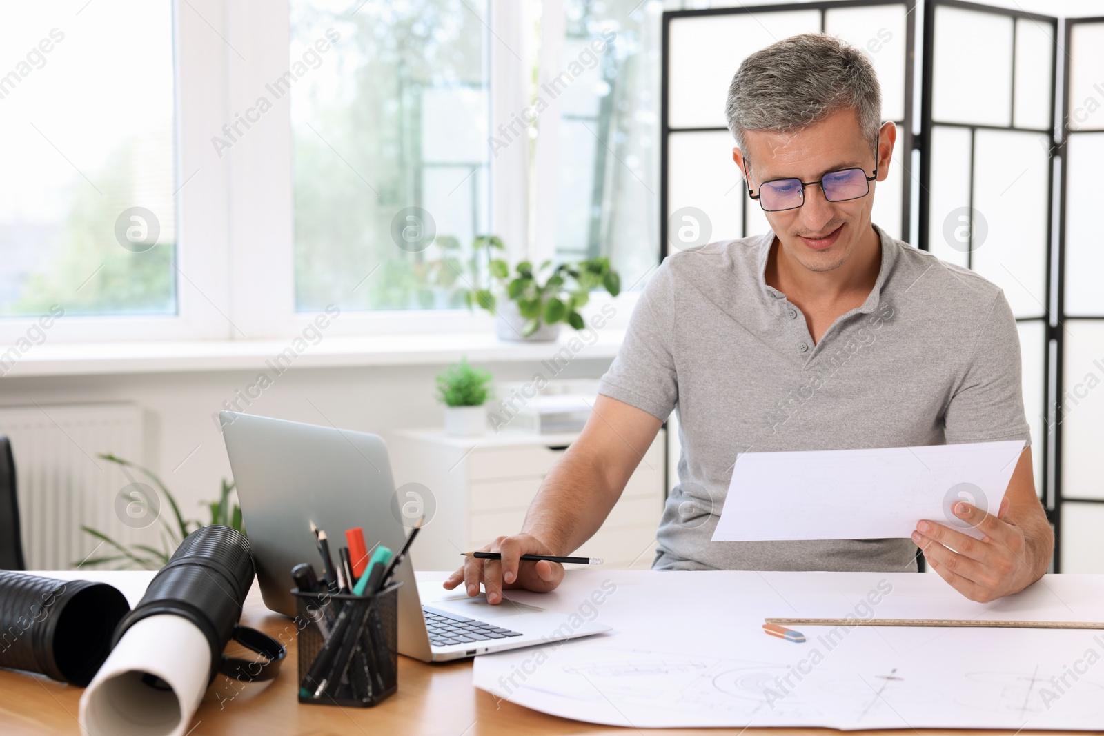 Photo of Architect with engineering drawing at wooden table in office