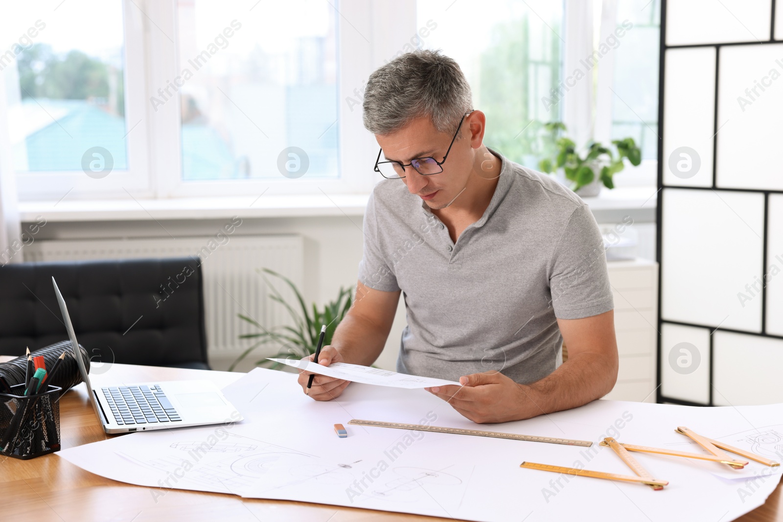 Photo of Architect with engineering drawing at wooden table in office