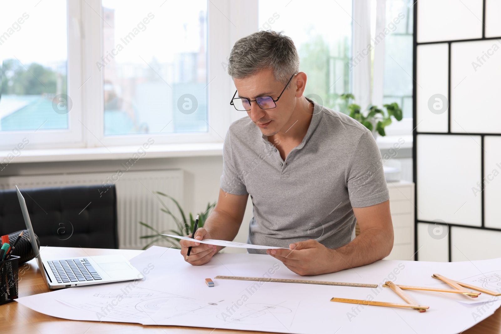 Photo of Architect with engineering drawing at wooden table in office