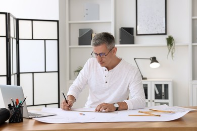 Photo of Architect making engineering drawing at wooden table in office