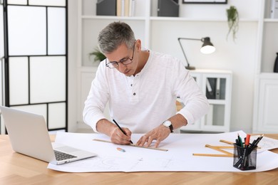 Photo of Architect making engineering drawing at wooden table in office