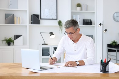 Photo of Architect making engineering drawing at wooden table in office