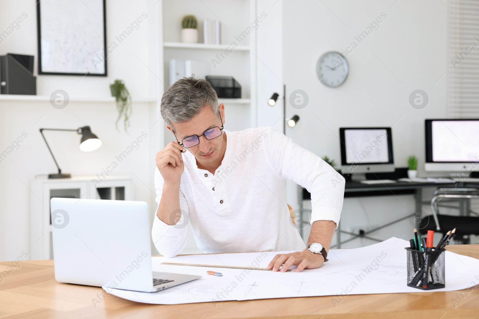 Photo of Architect making engineering drawing at wooden table in office