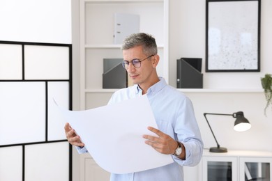 Architect holding paper sheet with engineering drawing in office