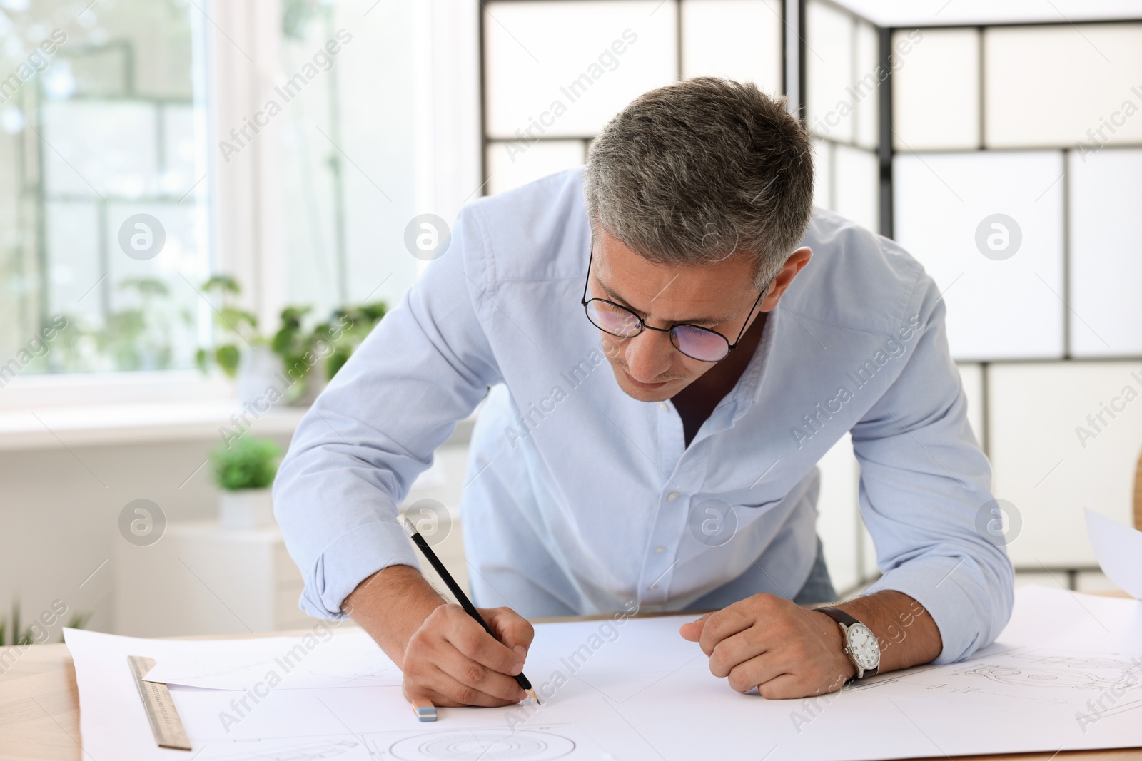 Photo of Architect making engineering drawing at wooden table in office