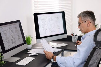 Photo of Architect checking engineering drawing at table in office