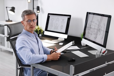 Architect checking engineering drawing at table in office