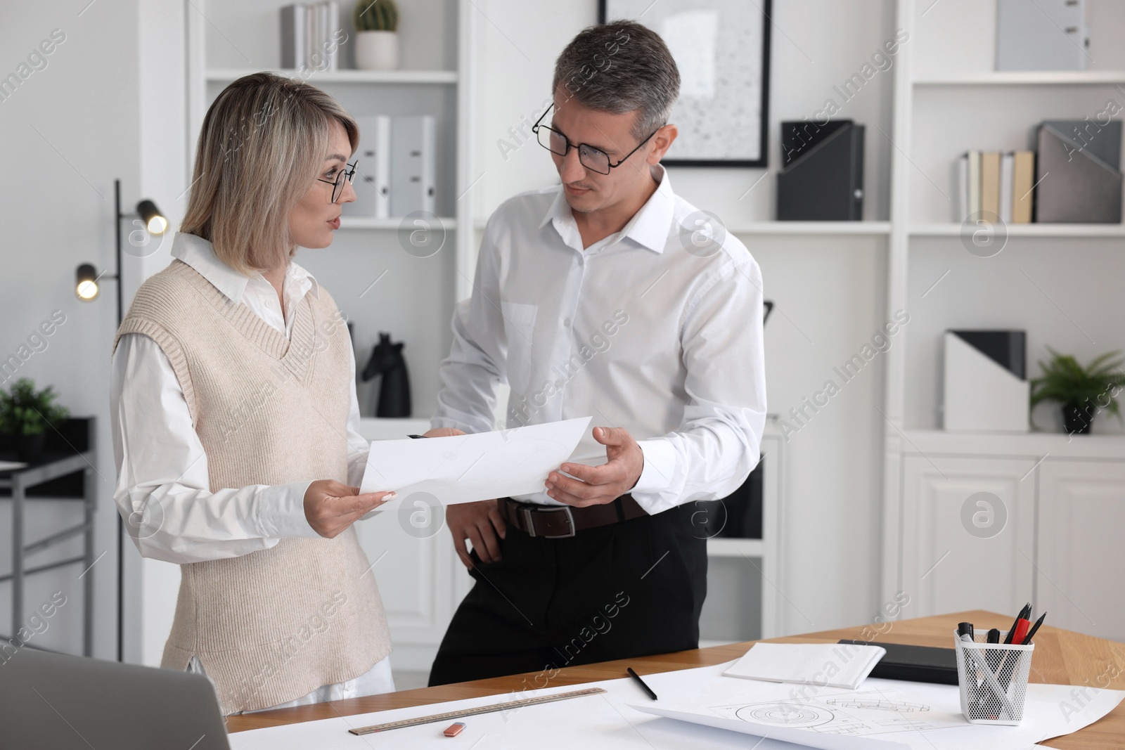 Photo of Architects discussing engineering drawing at wooden table in office