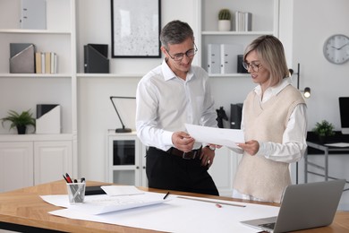 Photo of Architects discussing engineering drawing at wooden table in office