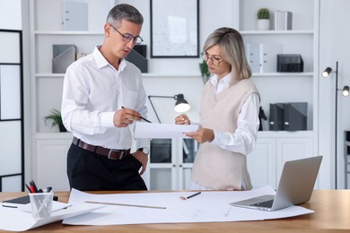 Architects discussing engineering drawing at wooden table in office