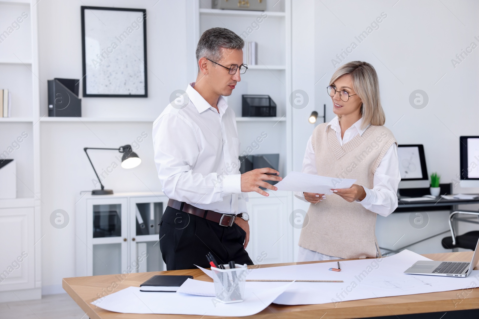 Photo of Architects discussing engineering drawing at wooden table in office