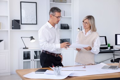 Architects discussing engineering drawing at wooden table in office