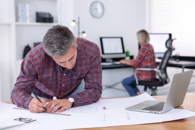 Photo of Architect making engineering drawing at wooden table in office