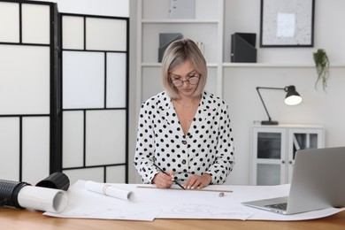 Photo of Architect making engineering drawing at wooden table in office