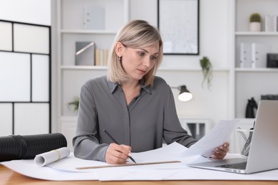 Architect making engineering drawing at wooden table in office