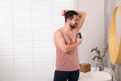 Photo of Smiling man applying roll-on deodorant near mirror at home. Space for text