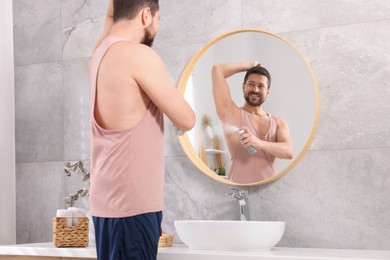 Photo of Smiling man applying spray deodorant near mirror at home