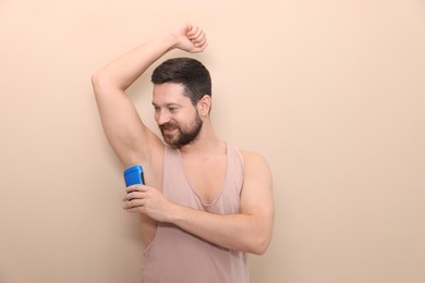 Smiling man applying solid deodorant on beige background