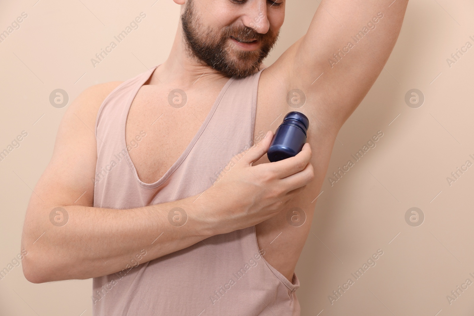 Photo of Man applying roll-on deodorant on beige background, closeup