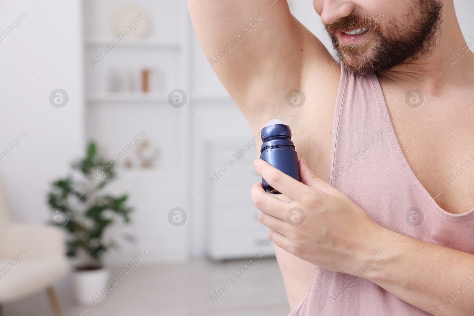 Photo of Man applying roll-on deodorant at home, closeup. Space for text