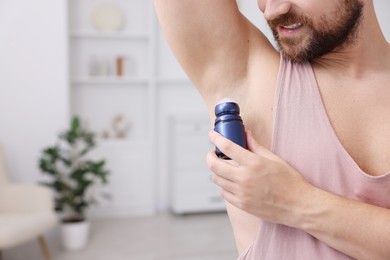 Man applying roll-on deodorant at home, closeup. Space for text