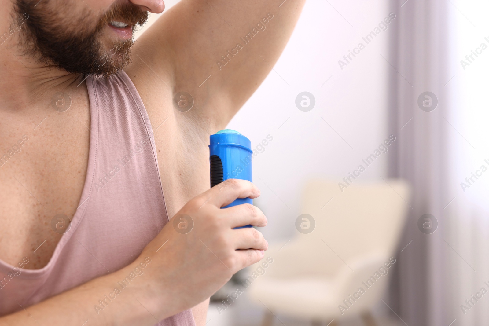 Photo of Man applying solid deodorant at home, closeup. Space for text