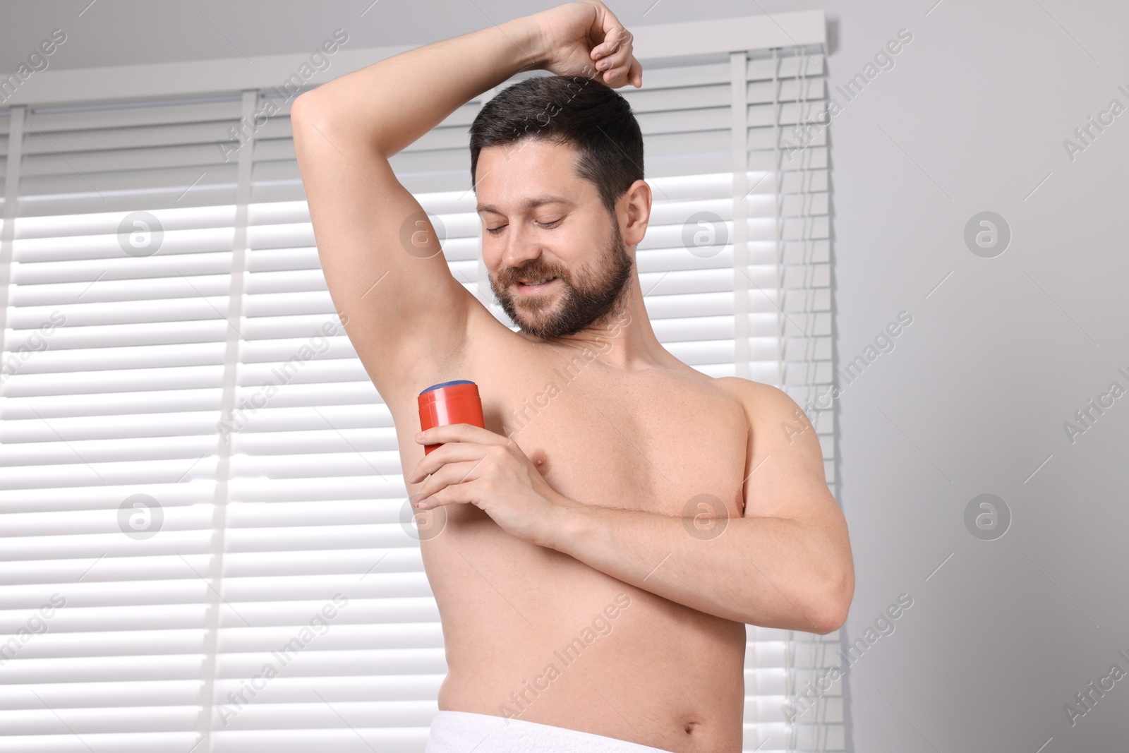 Photo of Smiling man applying solid deodorant at home