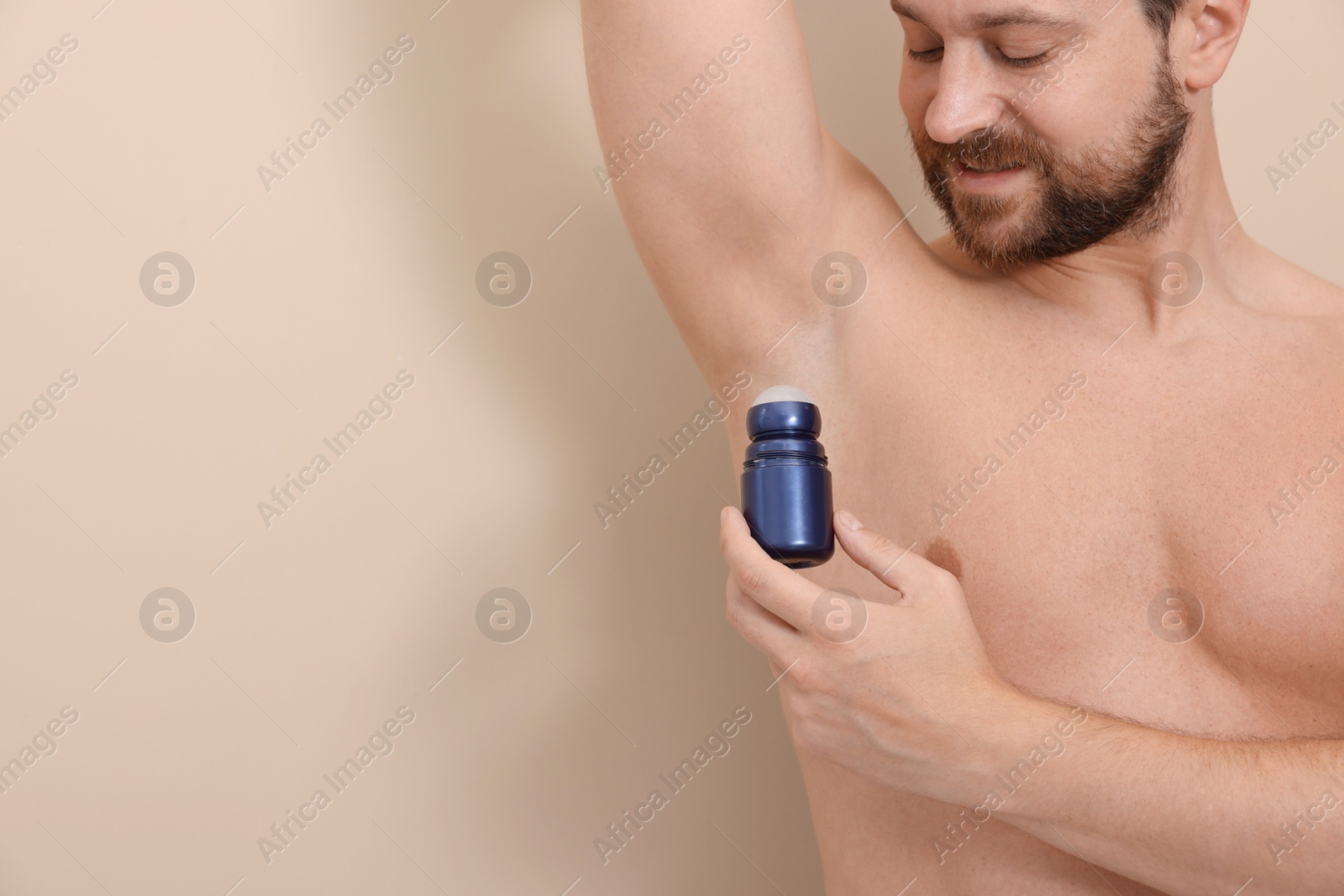 Photo of Man applying roll-on deodorant on beige background, closeup. Space for text