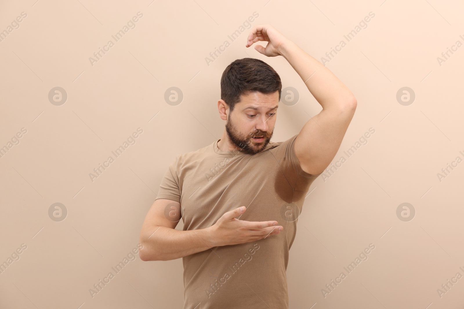 Photo of Emotional man in t-shirt before using deodorant on beige background